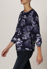 Blusa a stampa floreale in navy e bianco, con maniche 3/4, scollo rotondo e vestibilità comoda. Tessuto morbido e testurizzato con modelli dettagliati.