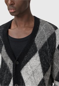 Cardigan à motif argyle en mélange de laine noire et grise, avec un col en V, une fermeture à bouton et un tissu doux et texturé.