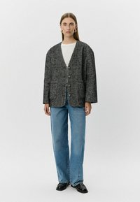 Černobílý herringbone blazer s volným střihem, dvěma předními kapsami a hlubokým výstřihem do V. Spárované se světle modrými širokými džínami.