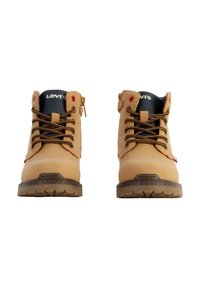 Bottines en cuir tan avec des accents noirs, des lacets marron et un marquage rouge. Elles présentent une semelle texturée pour une meilleure adhérence et un col rembourré pour le confort.