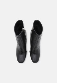 Botas de tobillo de cuero negro con un diseño elegante, que cuentan con un cierre lateral y punta redonda. La textura es suave con un acabado mate.
