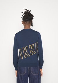 Suéter azul marino con "IKKE" bordado en amarillo en la parte posterior. Hecho de tejido de punto, presenta mangas largas y puños acanalados.