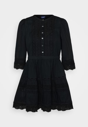 Must mustvalgest riietus, millel on täiskleit, ümmargune kaelus, ees nupud ja pitsdetailid varrukatel ja servadel. Omab vormitud rinda.