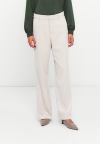 Pantalons en velours côtelé beige avec une coupe droite, dotés d'un devant plat et de passants de ceinture. Associés à un chemisier vert foncé et des talons hauts.