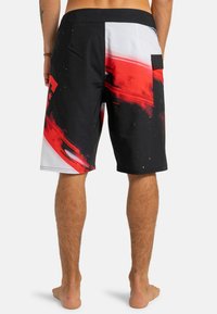 Čierne a červené šortky s abstraktnými farebnými škvrnami, bielymi akcentmi a zadným vreckom so zavretím na klopu. Vyrobené z ľahkého materiálu.