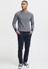 Suéter de punto texturizado en gris con mangas largas, combinado con pantalones ajustados de color azul marino oscuro y zapatillas negras con detalles en blanco.