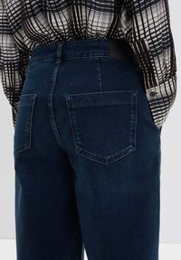 Donkerblauwe denim jeans met een hoge taille, met twee achterzakken en een zachte textuur. De tailleband heeft een zwart etiket.