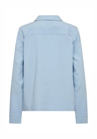 Camisa de manga larga de color azul claro con un acabado texturizado, puño abotonado y cuello clásico. La vista trasera muestra costuras suaves y un ajuste relajado.