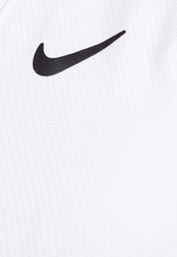Top atletico bianco con una texture a righe, caratterizzato da un logo Nike swoosh nero sul lato sinistro. Tessuto liscio, design minimale.