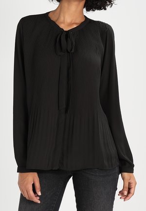 Blouse noire plissée avec un col rond, des manches longues et un détail à nouer à l'avant. Texture lisse, tissu léger.
