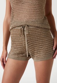 Pletený krémový crop top a odpovídající šortky s otevřeným vzorem. Obsahuje elastický pas se šnúrkou a texturovaný povrch.