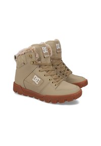 Beige Knöchelstiefel mit Kunstfellfutter, glänzendem synthetischem Obermaterial, Metallösen und robustem braunem Gummisohle. DC-Logo an der Seitenfläche.