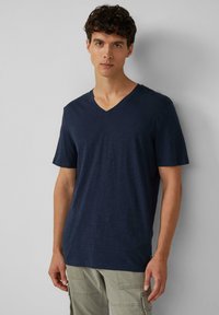 Granatowa bawełniana koszulka z dekoltem w kształcie V i krótkim rękawem; gładka faktura i luźny krój; z delikatnym melanżowym wzorem.