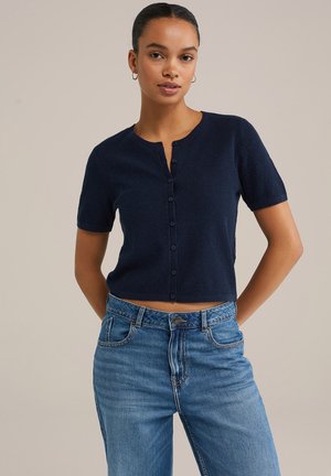 Marineblauer, kurzärmeliger Strickcardigan mit Rundhalsausschnitt und Knopfverschluss. Cropped-Schnitt, strukturiertes Gewebe, kombiniert mit hochtaillierten Jeans.