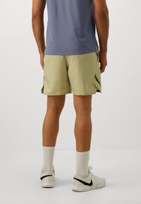 Grønne mønstrede shorts med løs pasform, sidelommer og kontrasterende brune detaljer. Kombineret med hvide sneakers og sokker.