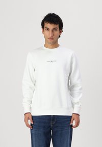 Biely crewneck sveter z bavlnenej zmesi s rebrovanými manžetami, ktorý má malé logo na hrudi a zvýrazňujúce pruhy na leme.
