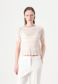 Crochetový top s krátkym rukávom v svetlej béžovej farbe, s jemnými vzormi, okrúhlym výstrihom a vlnitým okrajom na leme.