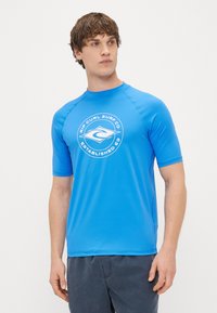 Zils īsām piedurknēm ar elastīgu materiālu, ar aplokšņu baltu logo, uz kura ir rakstīts "Rip Curl Surf Co" un "Established 69."