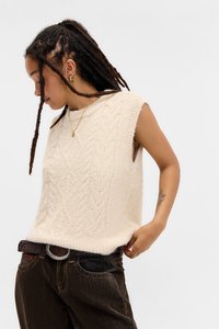 Strikket ærmeløs sweater i lys beige med et tekstureret kabelmønster. Bæret med mørk denim jeans og et tekstureret bælte.