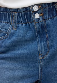 Blauwe denim broek met elastische tailleband en twee metalen knopen met het label premium quality denim.