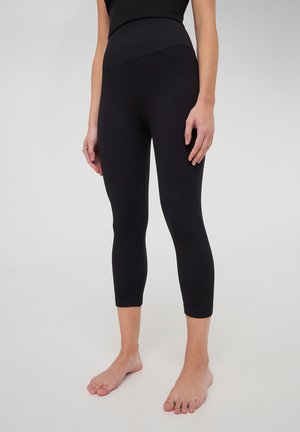Leggings neri a coste con vita alta e design aderente, che terminano poco sotto il polpaccio. Il tessuto testurizzato e i bordi senza cuciture sono visibili.