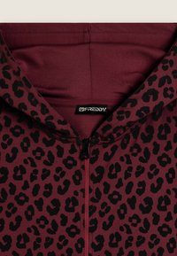 Sudadera con cremallera en burdeos que presenta un diseño de estampado de leopardo negro, fabricada con un tejido suave y con capucha forrada. Etiqueta del logo visible en el escote.