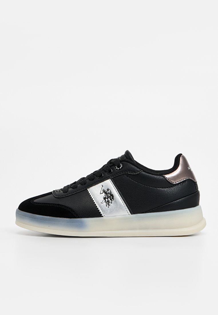 Zapatilla negra con materiales de cuero y sintéticos, franja plateada, suela de goma y logo bordado. Cuenta con un collar acolchado y cierre de cordones.