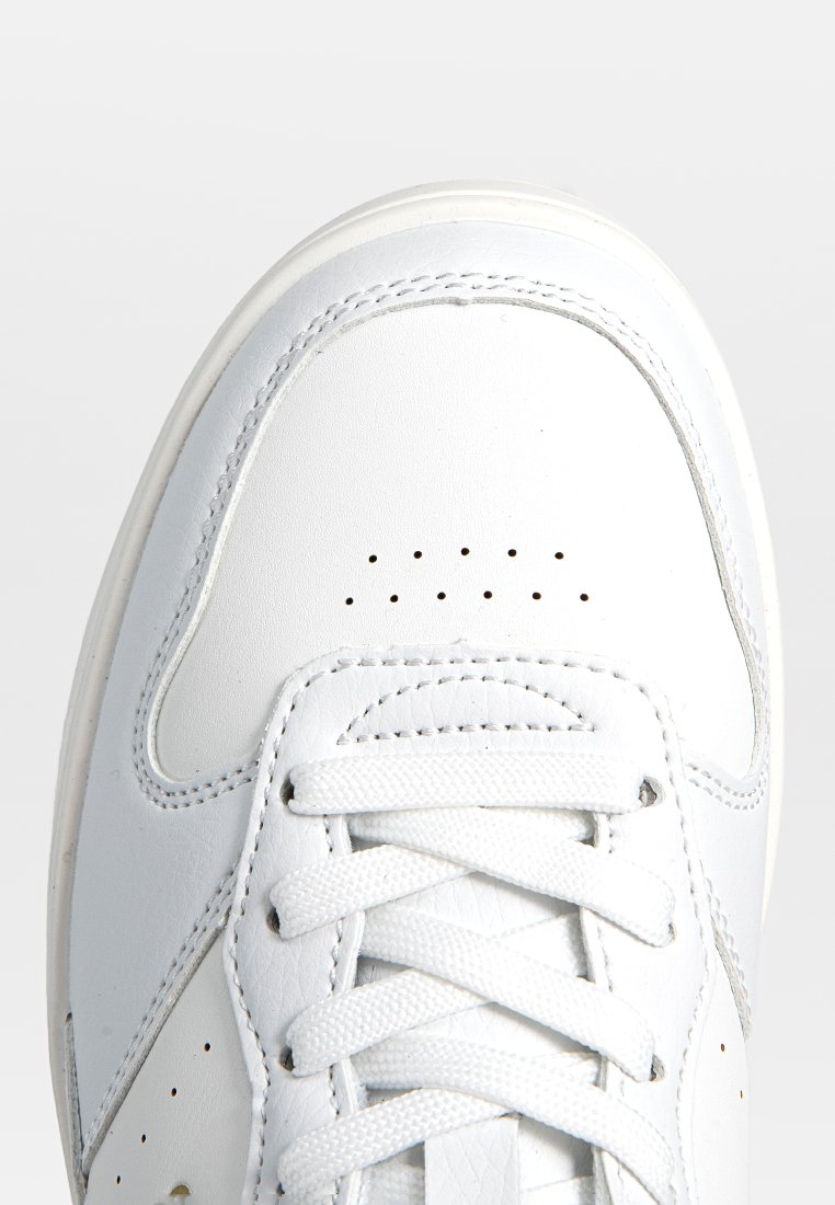 Sneaker bianco in pelle con punta arrotondata, dettagli perforati e lacci bianchi piatti. Presenta un design semplice e una suola leggera.