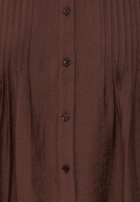 Tissu texturé marron avec des plis verticaux cousus et une rangée de cinq boutons marron foncé au centre.