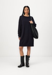 Vestido de suéter azul-marinho escuro com mangas longas, punhos canelados e decote arredondado. Combinado com botas de couro pretas até ao joelho e uma bolsa grande preta.