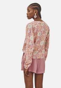 Top de manga larga con estampado floral en tonos pastel, combinado con pantalones cortos rosa claro. Presenta un corte holgado y una tela texturizada.