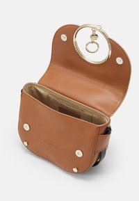 Borsa a tracolla in pelle marrone con manico circolare dorato, chiusura a scatto magnetico e interno in tessuto beige con una piccola tasca.