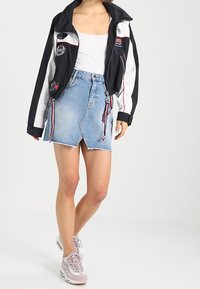 Jupe en denim avec ourlet effiloché, couleur bleu clair, et un design portefeuille. Associée à une veste zippée noire et blanche et des baskets roses.