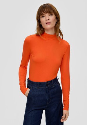 Oranje lange mouw turtleneck top gemaakt van zachte stof, gecombineerd met donkerblauwe high-waisted denim broek met twee knopen sluiting.
