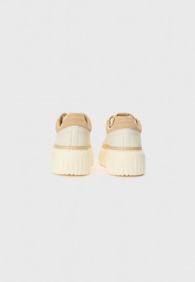 Baskets de sport beige avec une surface texturée, présentant un talon rond, une semelle plate-forme et des accents cousus dans une teinte plus claire.