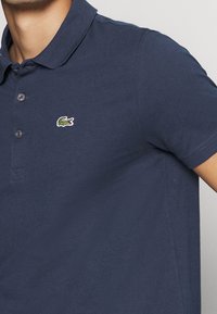 Polo shirt bleu marine avec un col côtelé, une patte de boutonnage à trois boutons et un logo crocodile brodé sur la poitrine gauche. Texture douce.