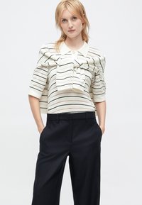 Knitted sweater with stripes in cream and black, featuring a collar and a large bow, paired with high-waisted black trousers.
