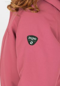 Roze jas met een gestructureerde stof, een getailleerde pasvorm en een zwart driehoekig Zigzag-logo op de bovenarm.