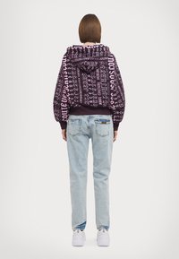Felpa viola con testo rosa, dotata di tasca frontale e coulisse. Abbinata a jeans azzurri chiari e sneakers bianche.