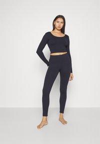 Námornícky modrý rebrovaný crop top s dlhým rukávom v kombinácii s legínami s vysokým pásom, oboje vyrobené z elastického materiálu, ktorý zvýrazňuje priliehavý siluetu.