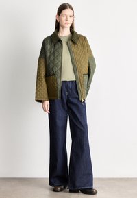 Πανωφόρι με χρωματιστές ραφές στο κολιέ, σχεδιασμένο σε ελιά πράσινο και καφέ, με γιακά και τσέπες με πάτσα, συνδυασμένο με φαρδιά τζιν παντελόνια και μαύρες μπότες.
