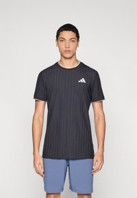 Maglietta sportiva nera con righe verticali, maniche corte e scollo rotondo bianco. Presenta un logo Adidas bianco sul petto a sinistra.