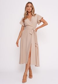 Wickelkleid aus beigem Stoff mit kurzen, schwingendenÄrmel, in der Taille gebunden, seitlichem Schlitz und fließender A-Linie.