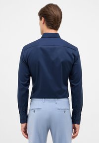 Camicia a maniche lunghe blu navy con texture liscia e colletto classico, abbinata a pantaloni azzurri chiari con due tasche posteriori e bottoni.