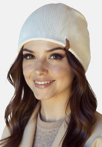 Kremowa dzianinowa czapka beanie o teksturowanym wykończeniu, z podwiniętym brzegiem i małą brązową skórzaną metką z boku.