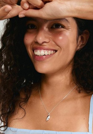 Silver pendant necklace featuring a smooth, leaf-shaped charm on a thin chain, worn by a person with curly hair, against a soft background.