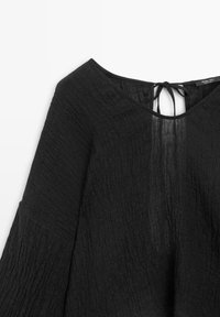 Sort tekstureret bluse med lange ærmer, vide ærmer, rund halsudskæring og bindelukning bagpå nær kraven.