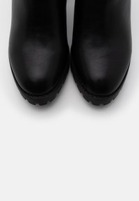 Botas de piel negras hasta el tobillo con punteras redondeadas, superficie texturizada y suelas de goma negra resistentes. Diseño simple sin herrajes visibles.