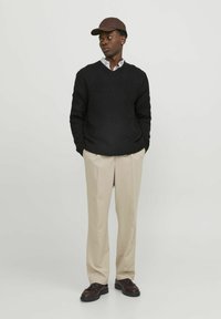 Black knitted sweater with a V-neck and textured pattern, beige trousers, brown cap, and dark shoes. The outfit has a casual, layered look.