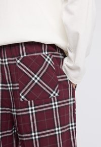 Bordeaux-geruite broek gemaakt van zacht materiaal, met een patchzak met witte en zwarte lijnen en een elastische tailleband.